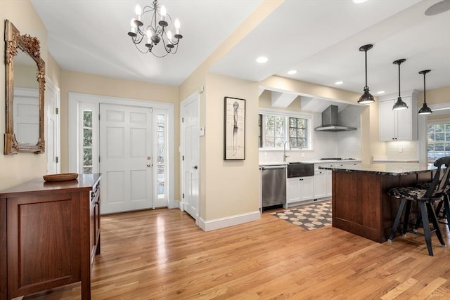 kitchen featuring hanging light fixtures, white cabinetry, stainless steel dishwasher, and wall chimney exhaust hood