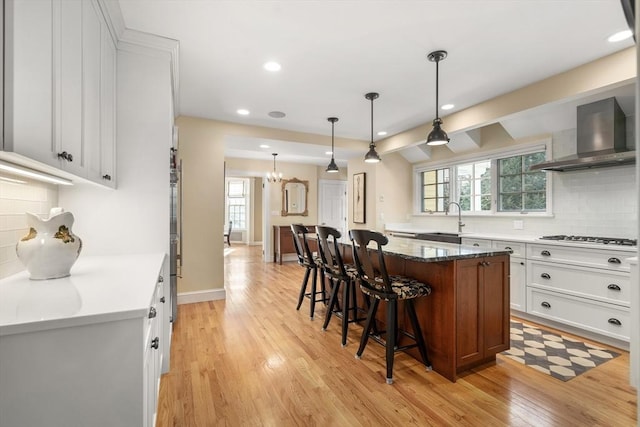 kitchen with white cabinetry, a center island, and wall chimney range hood