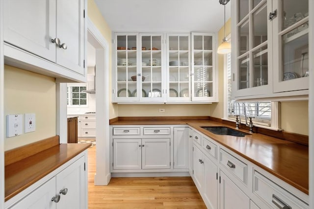 kitchen featuring wood counters, sink, white cabinetry, hanging light fixtures, and light wood-type flooring