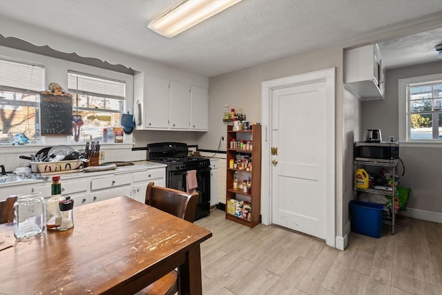 kitchen with white cabinetry, light hardwood / wood-style floors, gas stove, and a textured ceiling