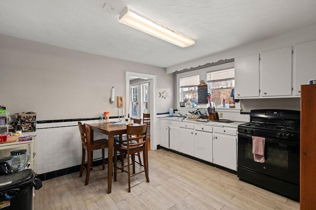 kitchen with black gas range, tile walls, white cabinets, and light wood-type flooring