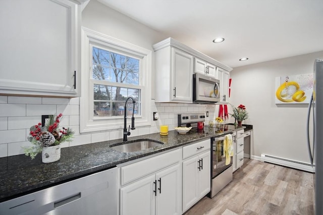 kitchen with white cabinets, dark stone countertops, stainless steel appliances, and a baseboard heating unit