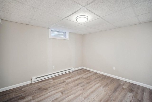 basement featuring a paneled ceiling, wood-type flooring, and a baseboard heating unit