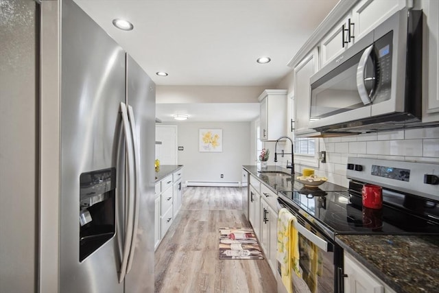 kitchen featuring backsplash, dark stone counters, white cabinets, light wood-type flooring, and appliances with stainless steel finishes