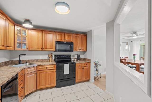 kitchen featuring black appliances, a sink, light tile patterned flooring, glass insert cabinets, and light countertops