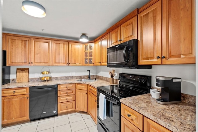 kitchen featuring black appliances, a sink, light tile patterned floors, glass insert cabinets, and light stone counters