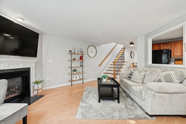 living room featuring stairway, light wood finished floors, a fireplace with flush hearth, and baseboards
