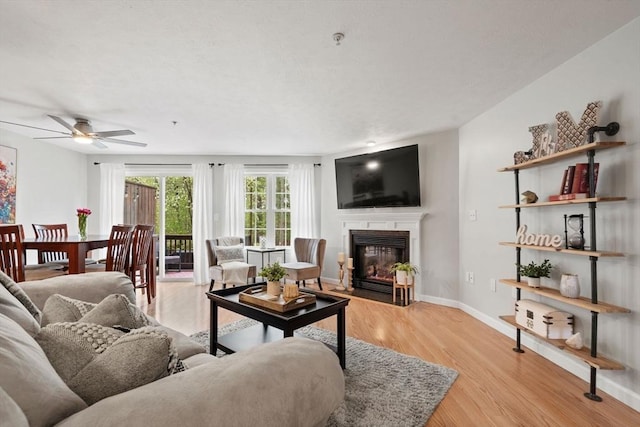 living area with a fireplace with flush hearth, a ceiling fan, light wood finished floors, and baseboards