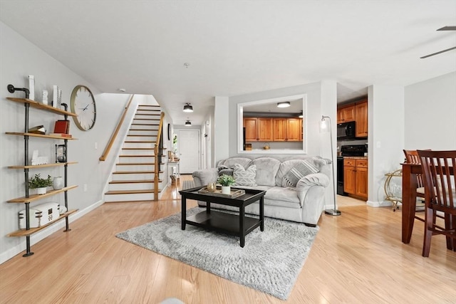 living room with a ceiling fan, stairway, light wood finished floors, and baseboards