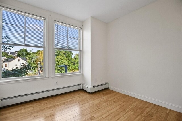 empty room featuring plenty of natural light, light wood finished floors, a baseboard heating unit, and baseboards
