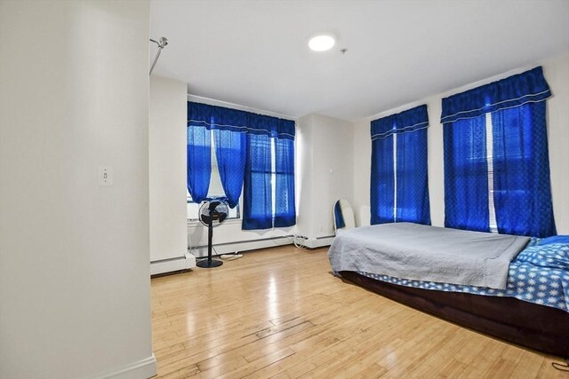 bedroom with baseboard heating, hardwood / wood-style flooring, and baseboards