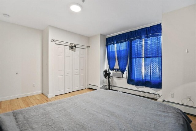 bedroom featuring baseboards, a baseboard heating unit, wood finished floors, and baseboard heating