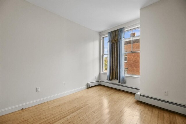 spare room featuring baseboards, a baseboard heating unit, and wood finished floors