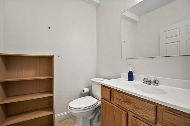 half bath with tile patterned flooring, vanity, baseboards, and toilet