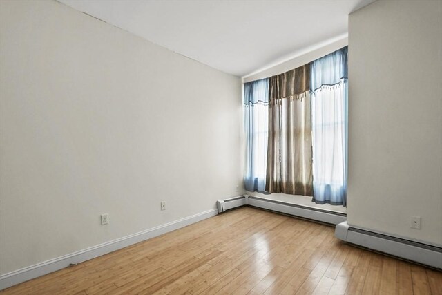 spare room featuring baseboard heating, a baseboard radiator, baseboards, and hardwood / wood-style flooring