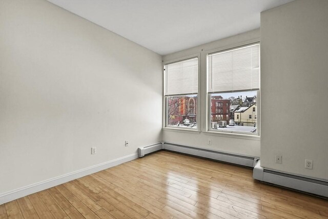 unfurnished room featuring a baseboard heating unit, hardwood / wood-style flooring, and baseboards