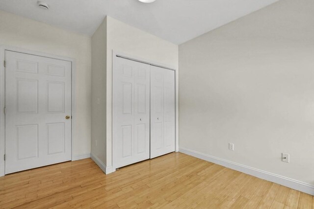 unfurnished bedroom featuring light wood-style flooring, a closet, and baseboards