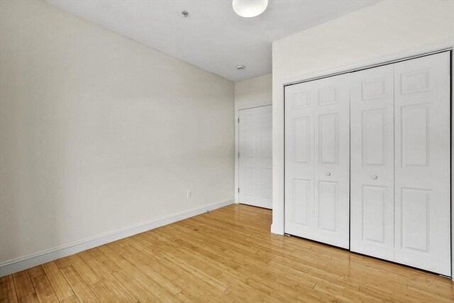 unfurnished bedroom featuring a closet, light wood-type flooring, and baseboards