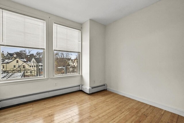 spare room with a baseboard heating unit, light wood finished floors, and baseboards