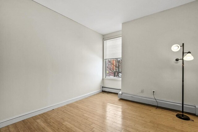 unfurnished room featuring a baseboard heating unit, baseboards, and wood finished floors