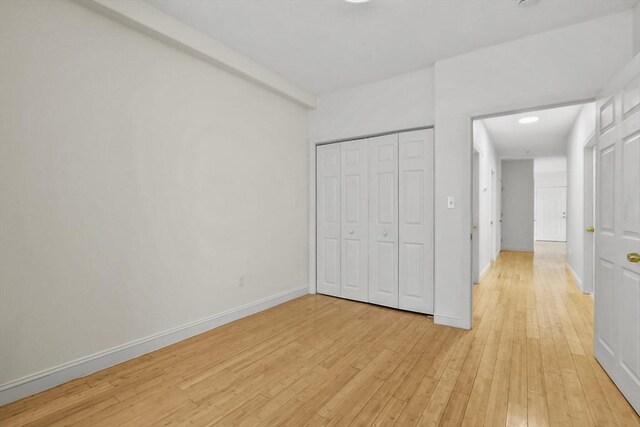 unfurnished bedroom featuring light wood-style flooring, a closet, and baseboards