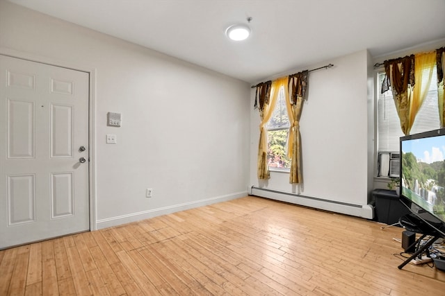 spare room with a baseboard heating unit, light wood finished floors, and baseboards