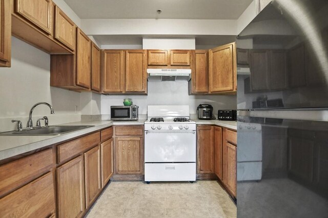 kitchen featuring a sink, gas range gas stove, under cabinet range hood, brown cabinets, and stainless steel microwave