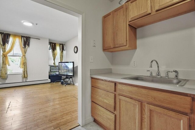 kitchen with light countertops, light wood-style flooring, a baseboard heating unit, and a sink