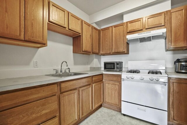 kitchen with a sink, light countertops, gas range gas stove, under cabinet range hood, and stainless steel microwave