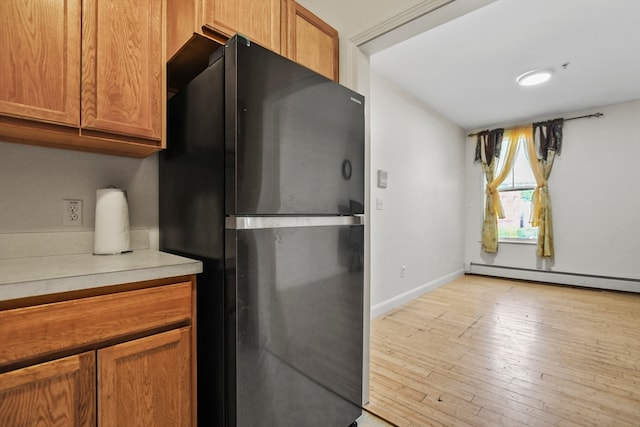 kitchen featuring a baseboard heating unit, light hardwood / wood-style floors, and black fridge