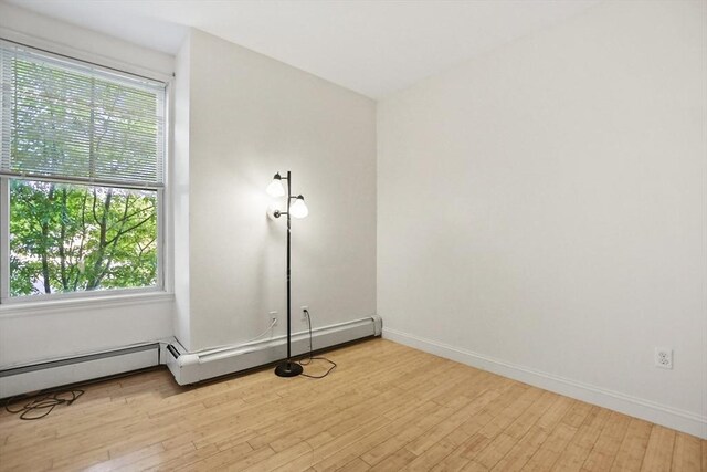 spare room with a baseboard radiator, wood finished floors, and baseboards