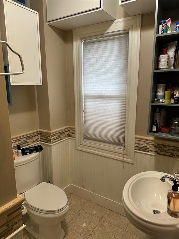 bathroom featuring tile patterned floors, toilet, a wainscoted wall, and a sink