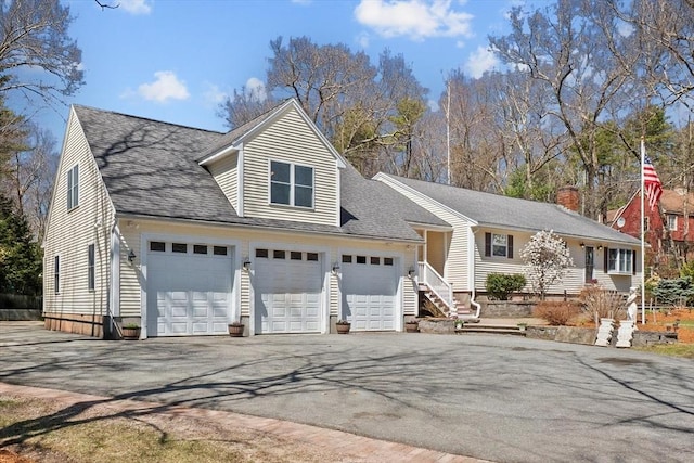 view of front of property featuring driveway, a garage, a shingled roof, and a chimney
