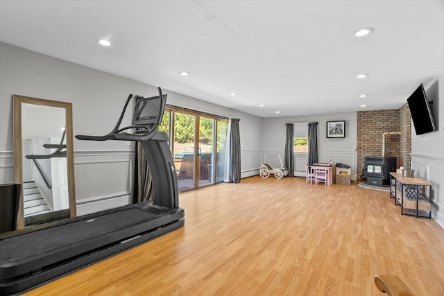 workout area with a decorative wall, light wood-style floors, a wood stove, recessed lighting, and wainscoting