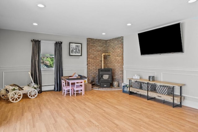 recreation room with a wood stove, a decorative wall, wood finished floors, recessed lighting, and baseboard heating