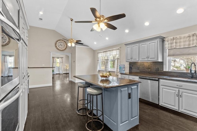 kitchen featuring a sink, stainless steel dishwasher, a ceiling fan, a center island, and dark wood finished floors