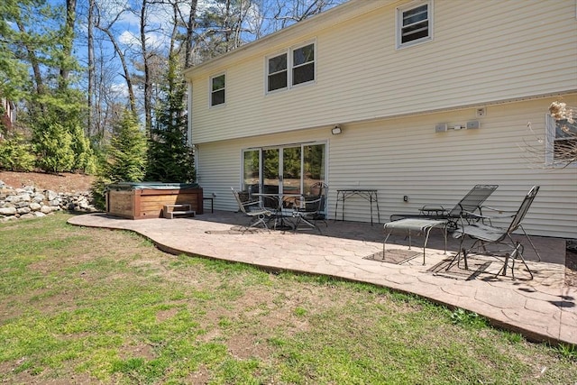 rear view of property featuring a hot tub, a patio area, and a lawn