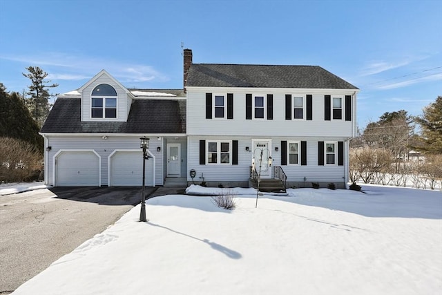 colonial house with an attached garage, a chimney, aphalt driveway, and roof with shingles