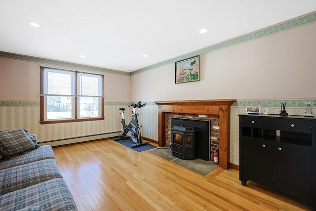 living room featuring wallpapered walls, wainscoting, a baseboard radiator, light wood-style flooring, and a wood stove