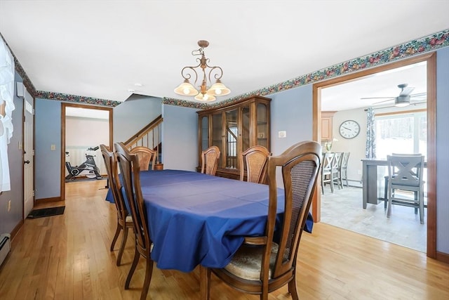 dining area featuring ceiling fan with notable chandelier, baseboards, baseboard heating, stairway, and light wood finished floors