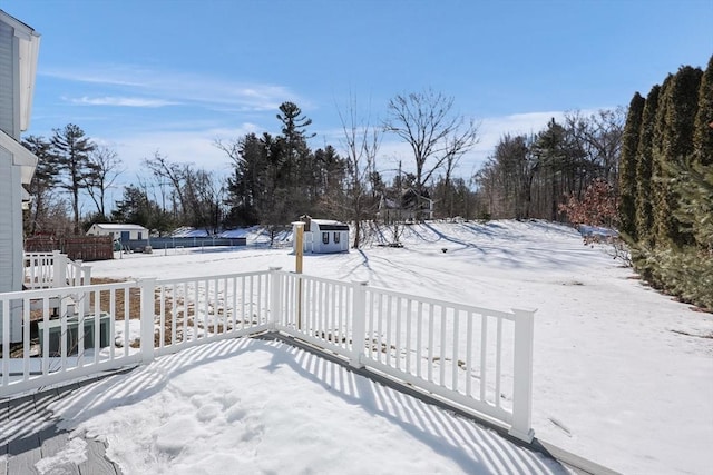 snowy yard featuring a storage shed, an outdoor structure, and fence