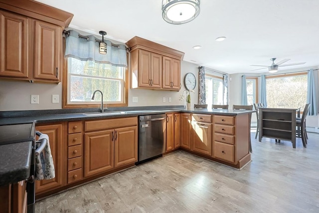 kitchen featuring dark countertops, stainless steel dishwasher, a sink, light wood-type flooring, and a peninsula