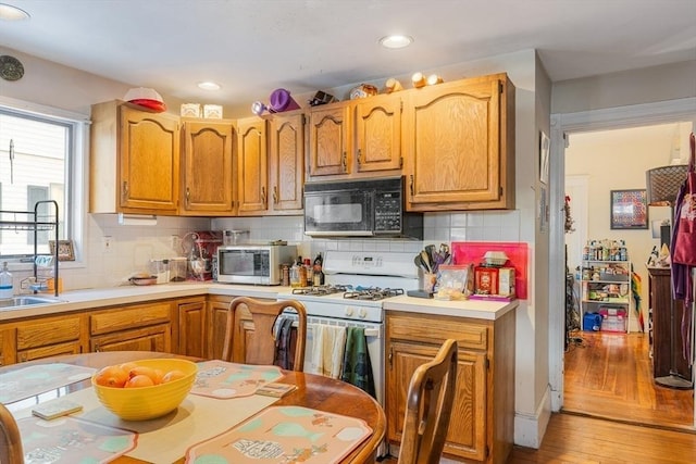 kitchen featuring sink, white gas stove, decorative backsplash, and light wood-type flooring