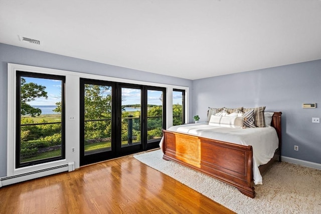 unfurnished bedroom featuring a baseboard heating unit, wood-type flooring, and multiple windows