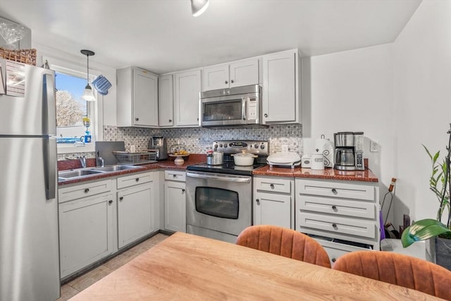 kitchen with appliances with stainless steel finishes, dark countertops, a sink, and tasteful backsplash