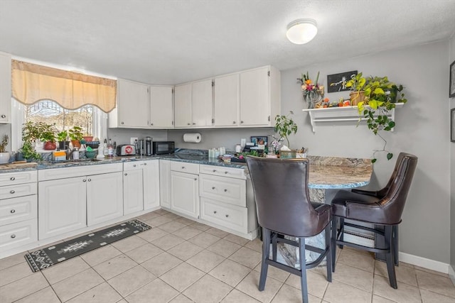 kitchen featuring black microwave, light tile patterned floors, a sink, white cabinetry, and baseboards