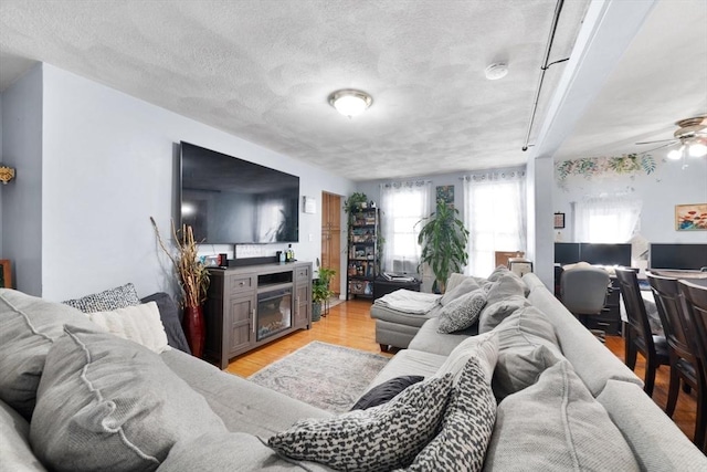 living room featuring ceiling fan, light hardwood / wood-style flooring, and a textured ceiling