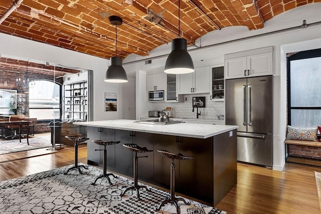 121-123 Beach St Unit 603, Boston, MA 02111 - kitchen with stainless steel appliances, brick ceiling, wood finished floors, white cabinets, and light stone countertops