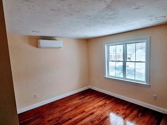 spare room with a textured ceiling, baseboards, an AC wall unit, and wood finished floors