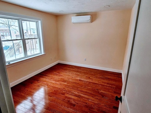 unfurnished room featuring hardwood / wood-style floors, a wall unit AC, and baseboards